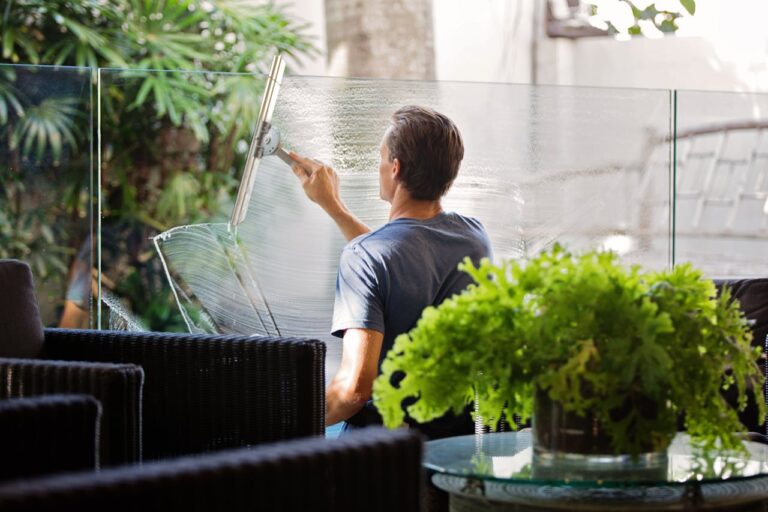 Hoteles impecables: aspectos clave de una limpieza profesional - 🧽 Limpieza y Orden – Trucos, consejos y servicios de limpieza cerca de ti A man cleaning a glass barrier outdoors with a squeegee, surrounded by greenery.